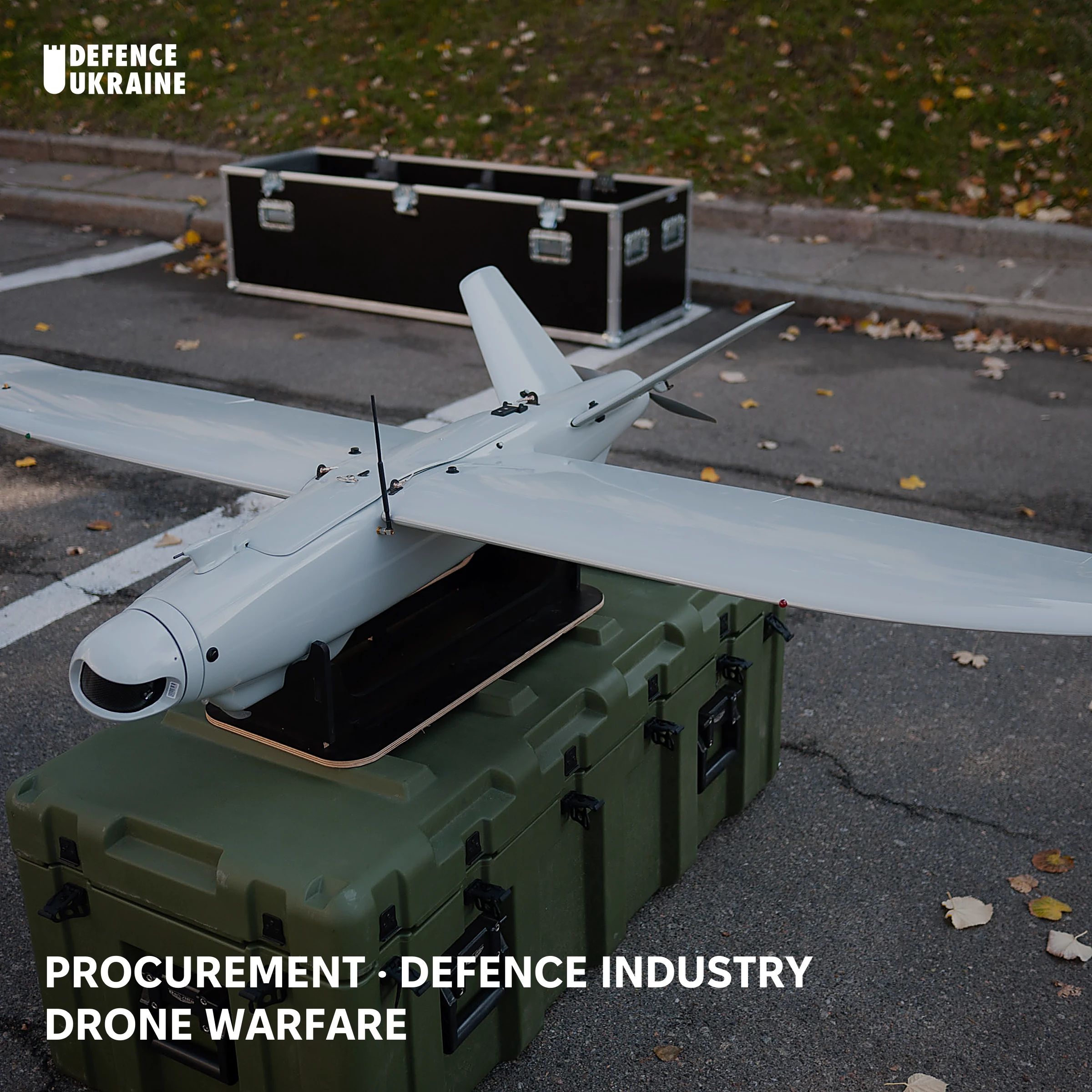 A Ukrainian-made Leleka-100 fixed-wing reconnaissance drone resting on its green transit case at a Kyiv military exhibition, presented as a catalogued item of supply alongside shipping crates.