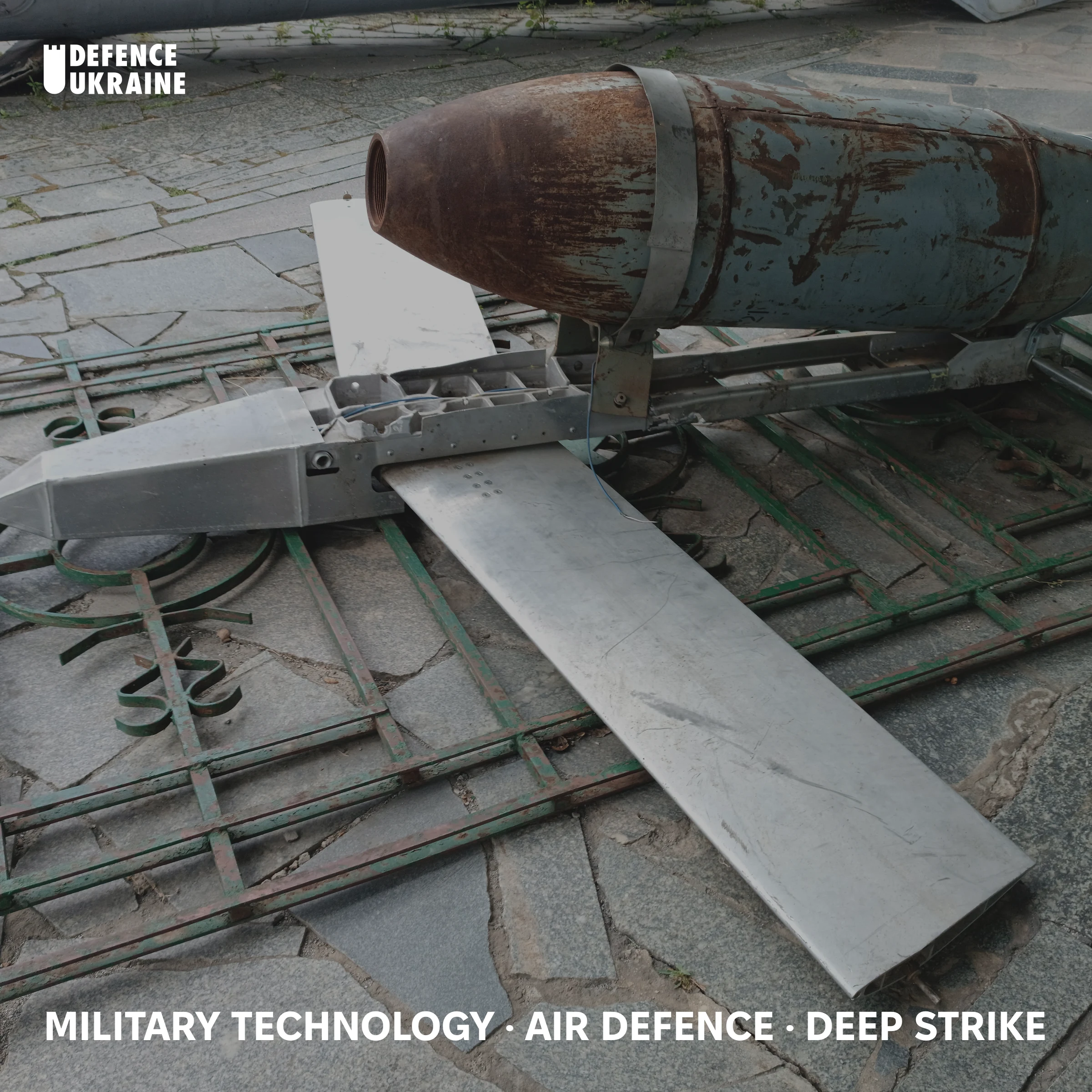 A captured Russian FAB-500 bomb fitted with a UMPK glide kit, displayed outdoors at a Kyiv museum, its rusted casing clamped to bare-metal wings and a guidance module.